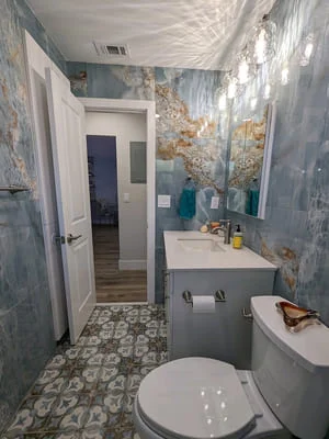 Bathroom with blue and gold tile walls, gray vanity, geometric floor tile, and white fixtures