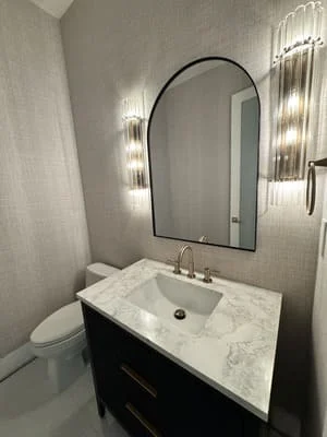 Marble vanity with black cabinet, arched mirror, and LED wall sconces in modern bathroom