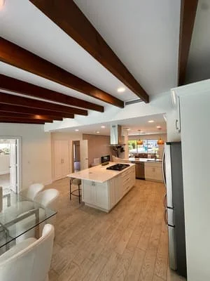 Open kitchen with white cabinetry, island, exposed wood beams, and wood flooring