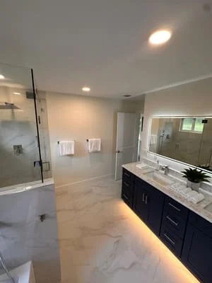Modern bathroom with marble flooring, frameless glass shower, dark vanity, and marble countertop