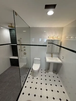 Frameless glass shower, white subway tile, black and white diamond floor pattern, pedestal sink