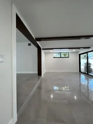 Open concept room with polished concrete floor, black exposed beams, white walls, and large windows