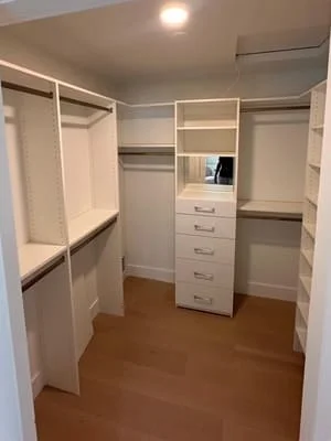 White custom closet system with hanging rods, central drawer tower, and shelving on wood flooring