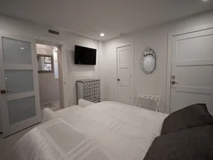 Master bedroom with white tile flooring, recessed lighting, and adjacent bathroom with glass shower enclosure