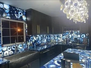Black kitchen cabinets with blue patterned tile backsplash, stainless steel counters, and crystal chandelier