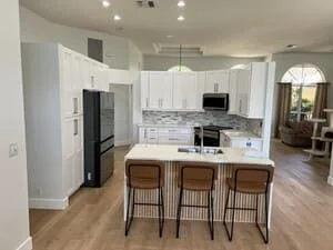 White kitchen cabinets, black stainless appliances, wood island with bar seating, hardwood floors