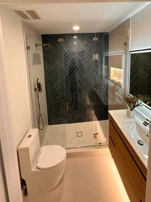 Modern bathroom with black herringbone tile shower, frameless glass door, floating wood vanity, and concrete flooring