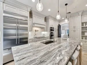 White kitchen with marble waterfall island, stainless steel appliances, and pendant lighting